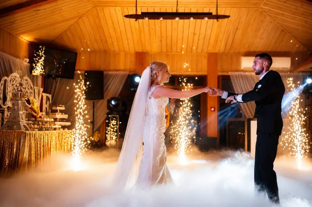 Bride and groom sharing their first dance surrounded by cold spark fountains and low-lying dry ice effects during a romantic wedding reception.