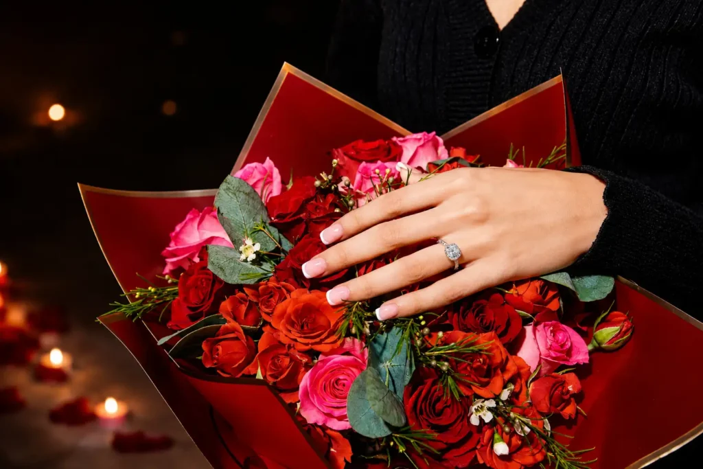Diamond engagement ring displayed on a woman's hand holding a luxury bouquet of red and pink roses during a romantic marriage proposal celebration in Dubai.