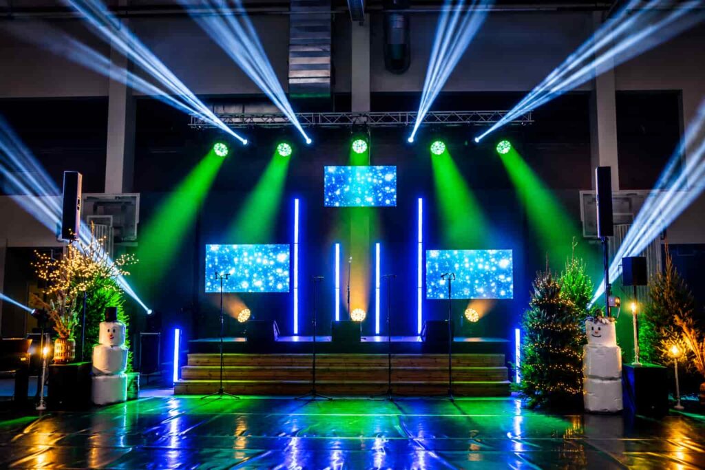 Professional event lighting setup in Dubai featuring moving head lights, LED screens, stage lighting, beam effects, illuminated Christmas décor, and a glossy dance floor for a corporate event or gala dinner.