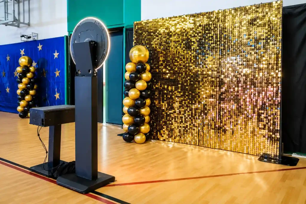 Box Entertainment's 360 photo booth with a gold shimmer sequin backdrop and black-and-gold balloon columns, set up for a school prom in Dubai, creating a stylish photo experience for students.