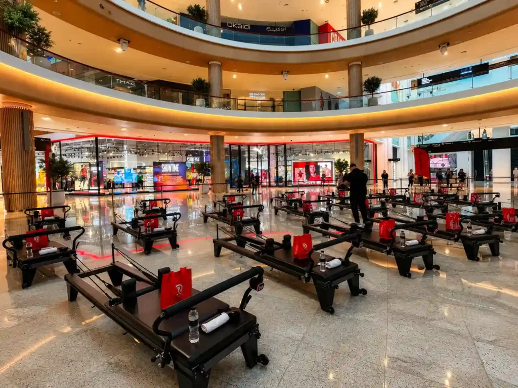 Pilates reformer machines arranged in a spacious shopping mall atrium for a wellness and fitness event, with premium workout equipment, branded accessories, and a modern retail environment in Dubai.