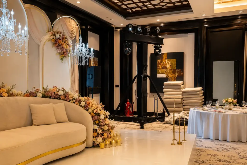 Luxury wedding stage setup in Dubai featuring elegant floral decor, a bridal sofa, decorative chandeliers, professional lighting truss, and event production equipment during the final stages of installation before guests arrive.
