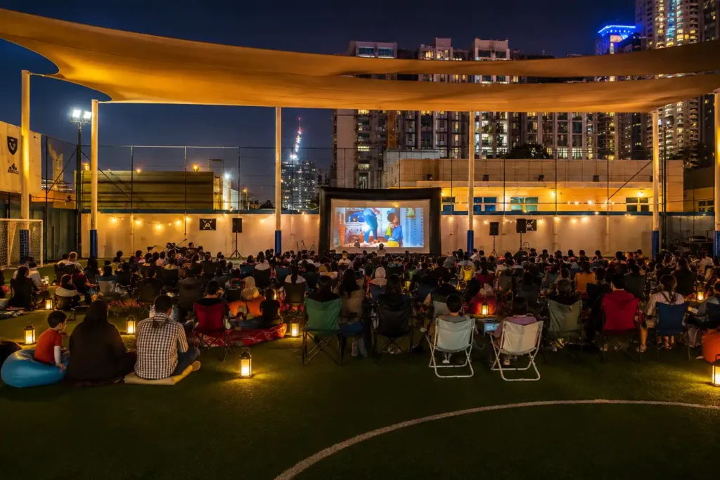 Outdoor cinema event in Dubai with a large movie screen, seated audience, professional sound system and city skyline at night.