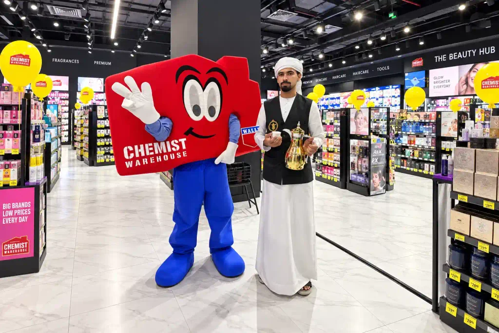 Chemist Warehouse mascot with an Emirati coffee server holding a traditional dallah during a store opening event in Dubai.
