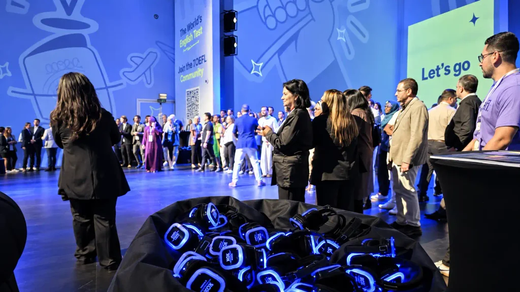 Blue illuminated wireless headsets in the foreground as guests gather at an indoor event in Dubai.