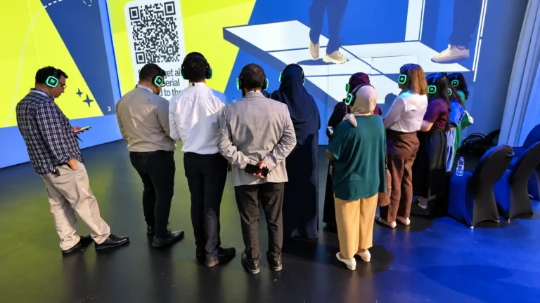 Guests wearing green-lit wireless headsets watch a projected presentation at an ETS MENA FZ LLC event in Dubai.
